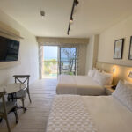 Image of bedroom area with two beds, a small table, two chairs and balcony in this condo in Surfside, Playa Caracol