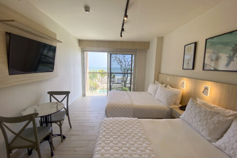 Image of bedroom area with two beds, a small table, two chairs and balcony in this condo in Surfside, Playa Caracol