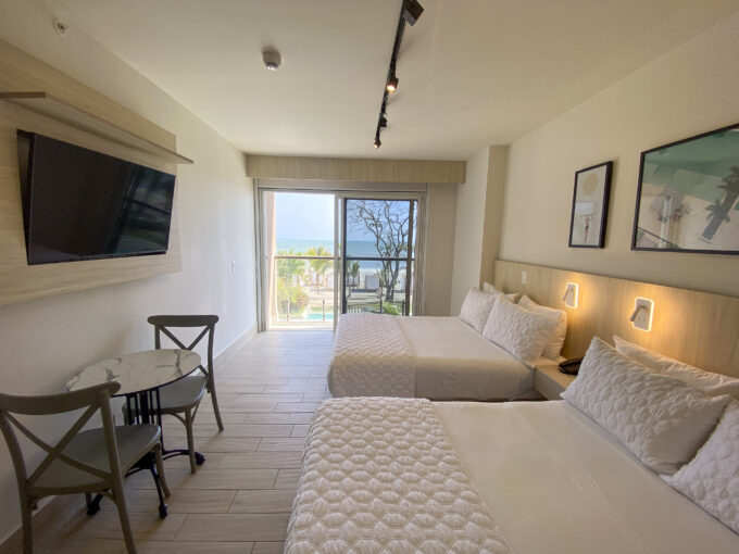Image of bedroom area with two beds, a small table, two chairs and balcony in this condo in Surfside, Playa Caracol