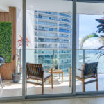 Image of the balcony with two chairs and a table looking out onto the ocean at Oasis on the Bay