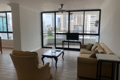 Image of the living area with balcony, table, television and two couches in this condo in Torre Mariluz