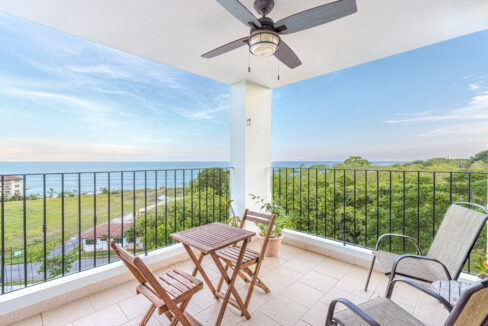 Image of balcony with two chairs, a table and chairs and views of the green spaces and ocean in this condo in Galeones