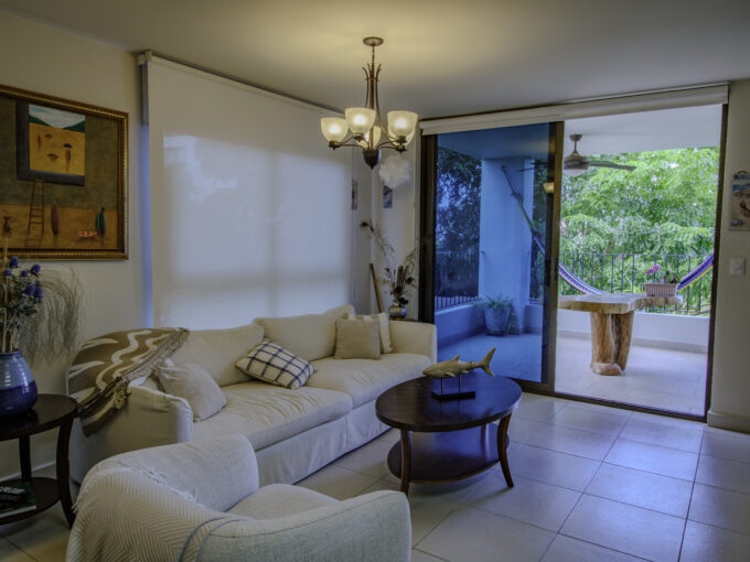Image of living area with couch and table leading onto balcony in this condo for sale in Galeones, Ensenada