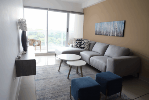 Image of living area with couch, tables and balcony in this furnished condo for sale in Residences del Sol