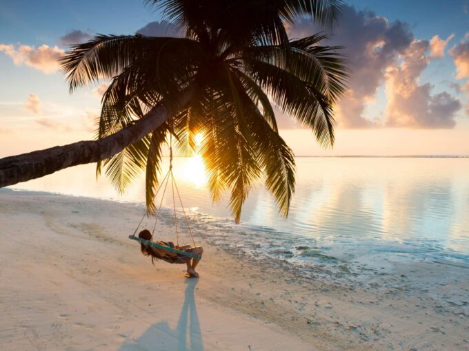 Person relaxing on a beach swing attached to a palm tree at sunrise showcasing Panama property management for foreign owners in Panamá City by Panama Equity Real Estate