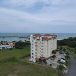 The Rocamarina building in Vista Mar seen from the air, with lawns, palms and the ocean behind it.