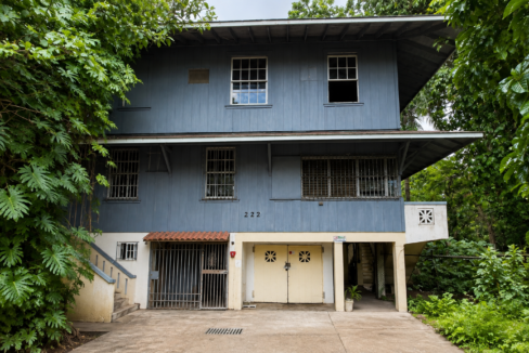 Two-story blue wooden teardown house on land for sale in Ancón, framed by large tropical plants