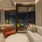 Living room at night in a Selvatica residence with a rust accent chair and glass doors onto the planted balcony.
