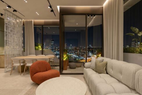 Living room at night in a Selvatica residence with a rust accent chair and glass doors onto the planted balcony.
