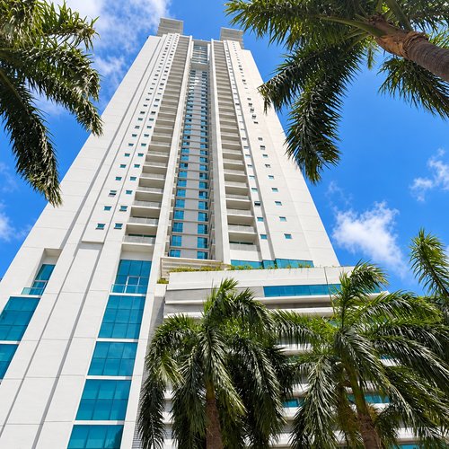 Looking up at a well-kept Panama City condo tower framed by palm trees